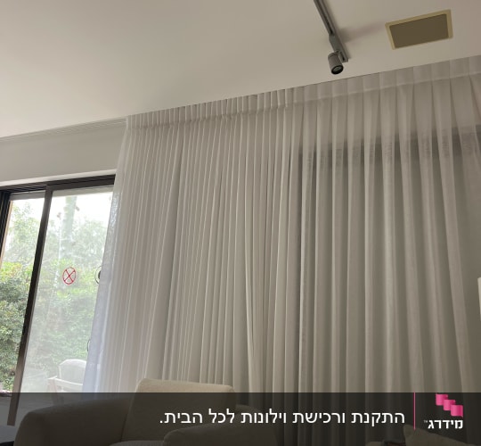 וילון לבן בסלון עם כורסאות ותאורה עליונה